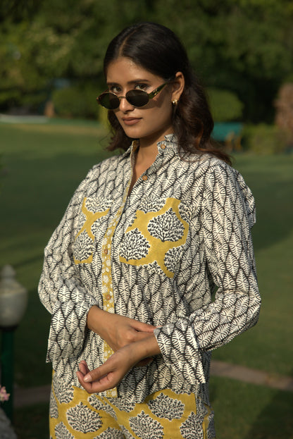 Woman wearing a patterned outfit with sunglasses against a blurred green background